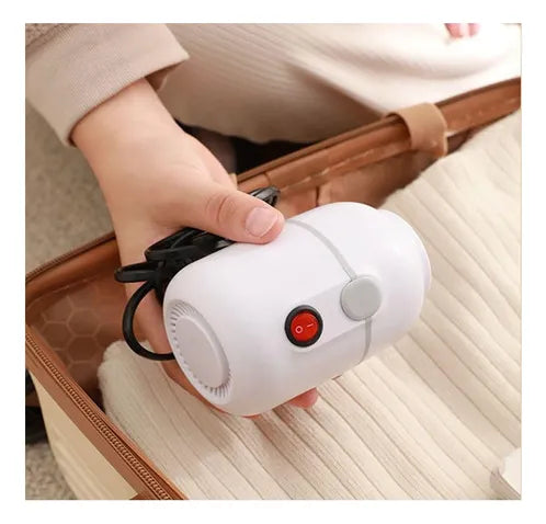 Bomba eléctrica para bolsas al vacío en la mano, junto a una maleta con ropa